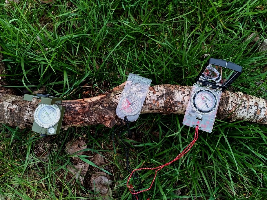 Alt:"Verschiedene Outdoormesser stehen vor einem mossbewachsenen Baumstamm"