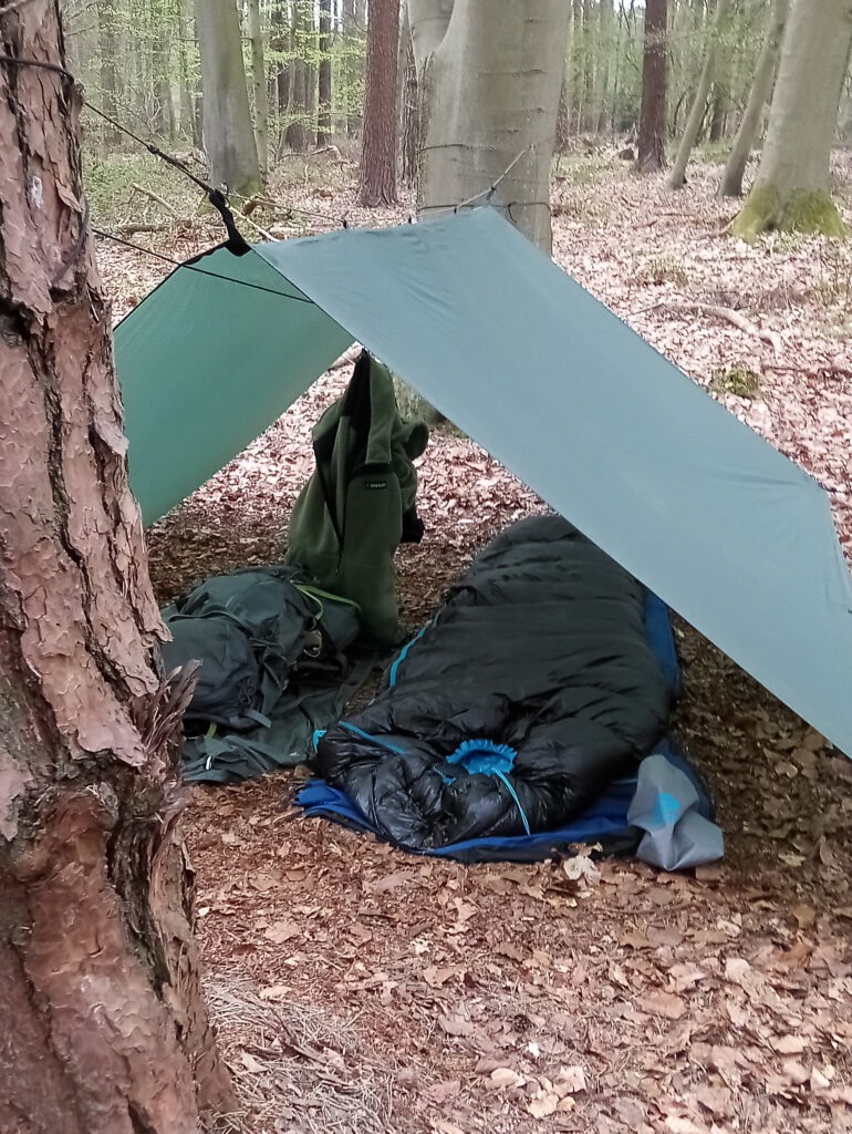 Daunenschlafsack unter Tarp im Wald – leichter Sommerschlafsack Survival